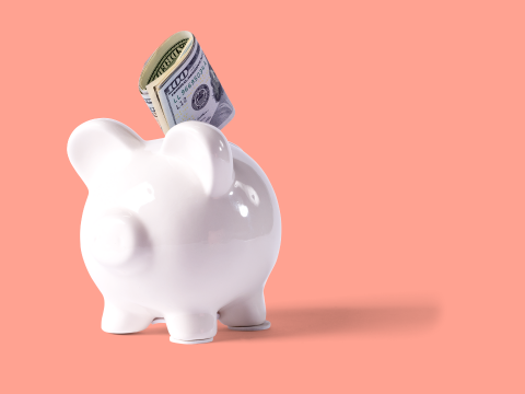 White piggybank with money going into it, in front of a peach colored background