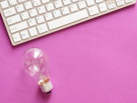 Keyboard and a lightbulb sitting on a purple background