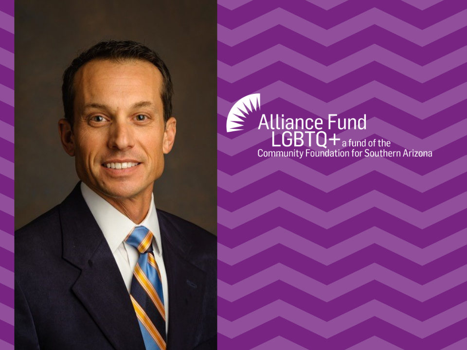 Photo of Kent Burbank wearing a dark suit and colorful tie in front of a purple patterned background.