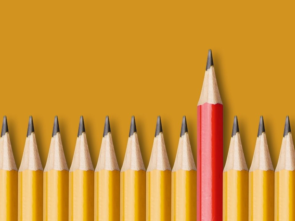 Yellow pencils in a row with one red pencil pushed higher up above the others.