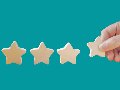 Four wooden stars with a hand placing them in a row.