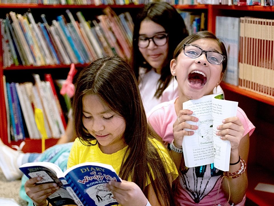 Children at a library joyfully holding and reading their books.