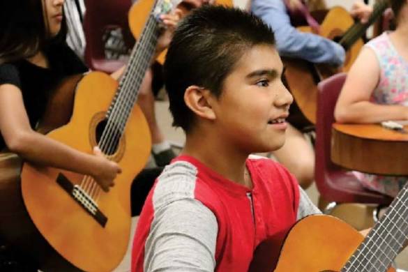 Child holding a guitar and smiling.