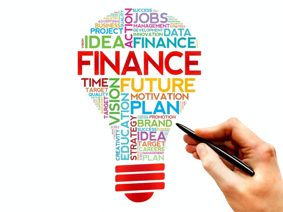 Colorful financial words shaped together to make a lightbulb, with a hand holding a pen near it