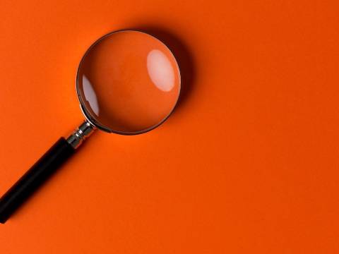 Magnifying glass in front of an orange background.