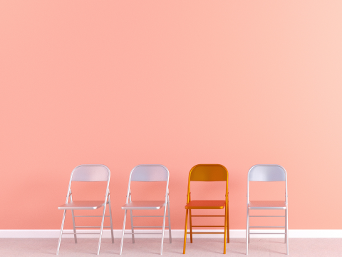 Three silver metal chairs and one red chair against a light pink background.