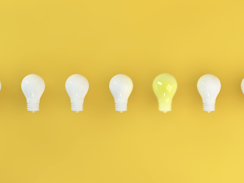row of lightbulbs with only one turned on in front of a yellow background