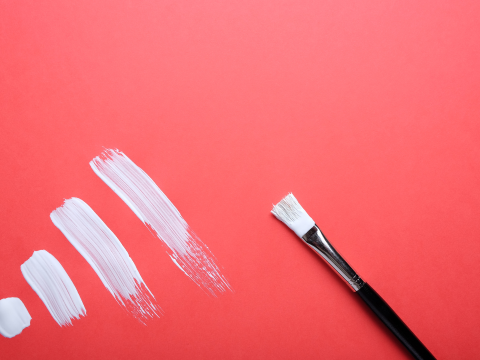 paint brush with white paint on it. In front of a pink background with white brushstrokes.
