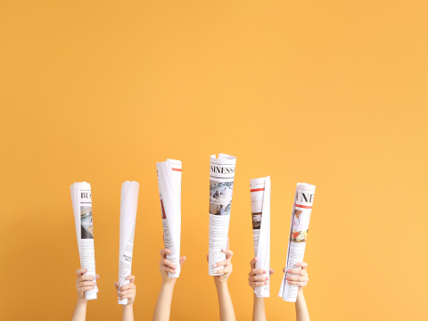 Six articles of newspaper being held up in front of an orange background
