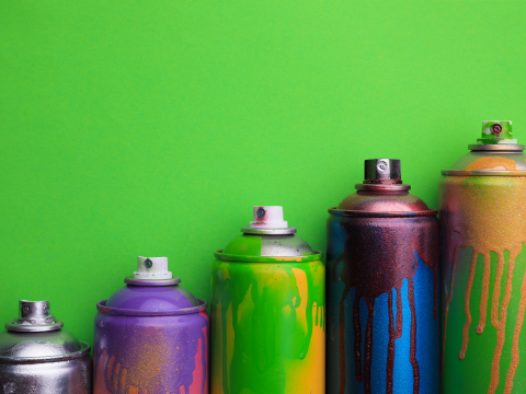 Used spray paint cans lined up in a row in front of a green background