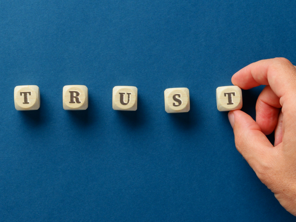 Hand placing small wooden blocks spelling out "trust" on a blue background