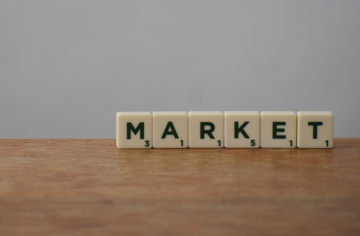 Scrabble tiles on a wooden table spelling out "market," with a gray background