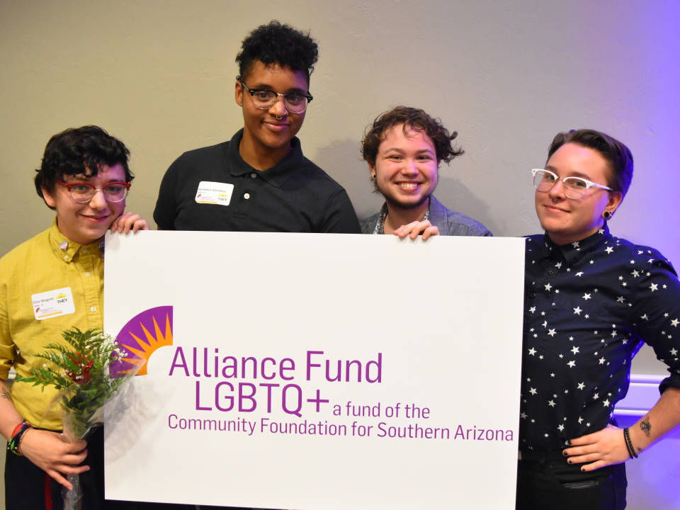 A group of four individuals holding a white sign that reads, "Alliance Fund LGBTQ+ a fund of the Community Foundation for Southern Arizona"