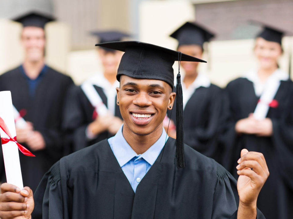Photo of Black man in black graduation cap and gown holding a diploma