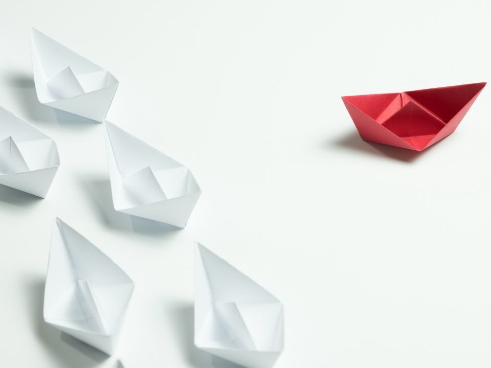 One Red and multiple white paper boats headed in different directions