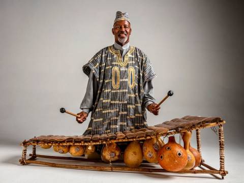 Man dressed in traditional attire in front of a wooden, traditional instrument